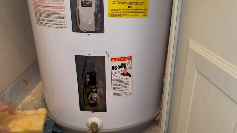 Electric water heater with access panels showing thermostat and element wiring before installation work